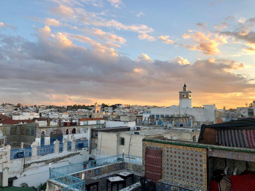 Daniel Speck Piccola Sicilia: Die Stadt Tunis ist in ein warmes weiches Licht getaucht. Man blickt auf ihre Dächer und Dachterrassen. Positive Farben und Muster unterstreichen die eindrucksvolle Kulisse.