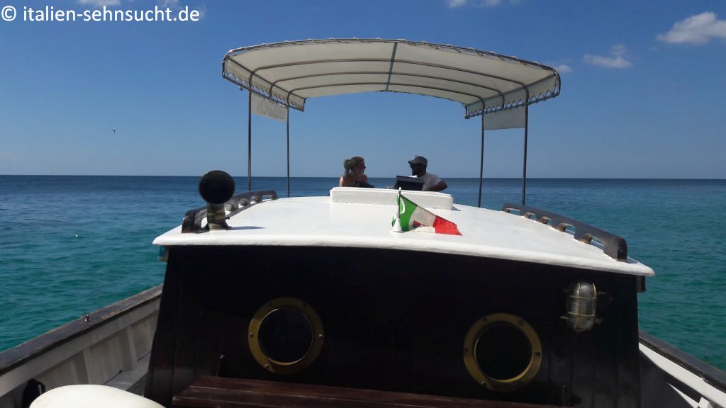 Strahlend blauer Himmel, türkisfarbenes Meer. Auf Deck Vanessa im Gespräch mit Davide de Giorgi, im Vordergrund eine italienische Flagge. 