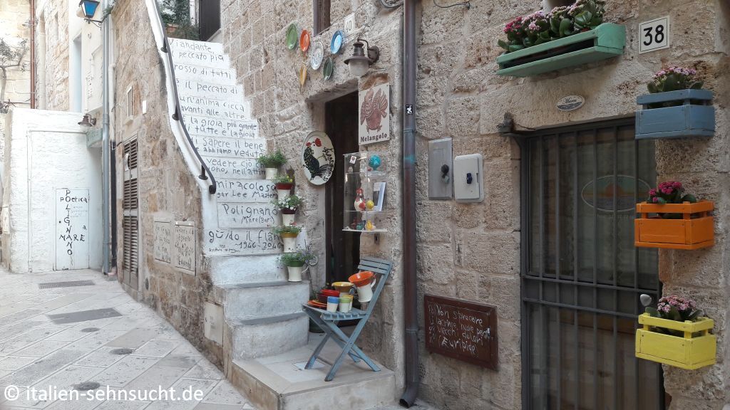Eine schmale Treppe schmiegt sich an eine Hauswand, Guido Luporis Schriften wandern über die Stufen, Blumentöpfe und bunte Dekoobjekte zieren die Kulisse.